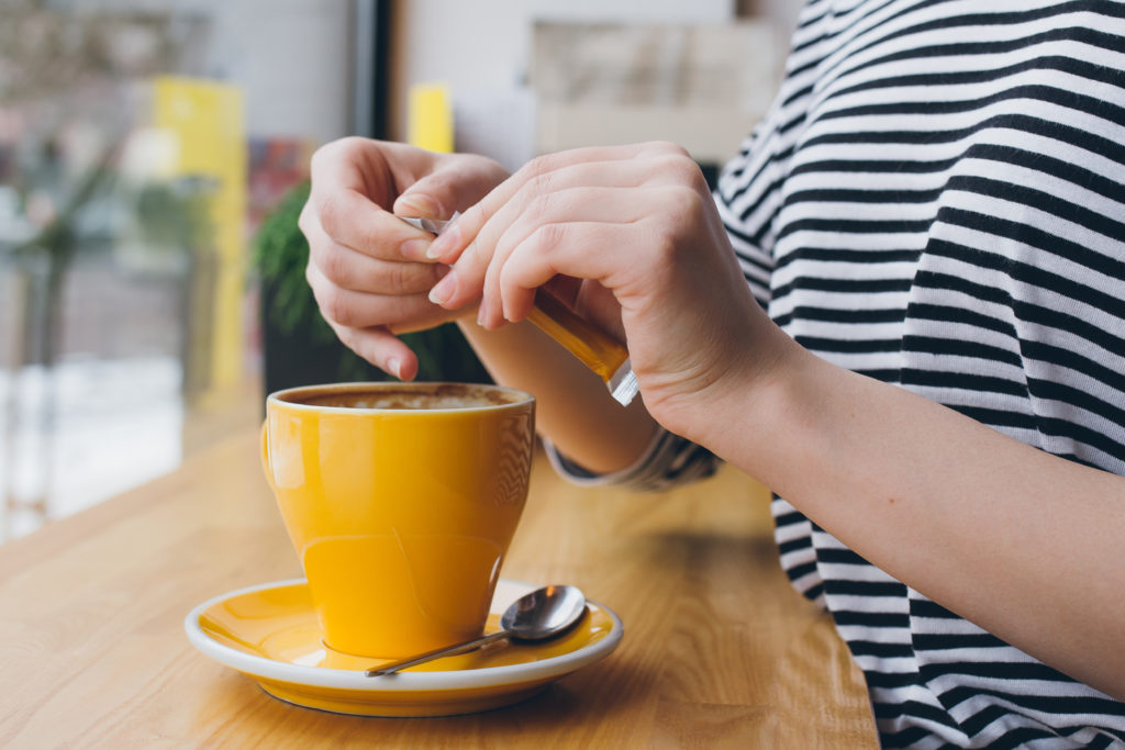 Close of up hands pours sweetener from a packet into a mug