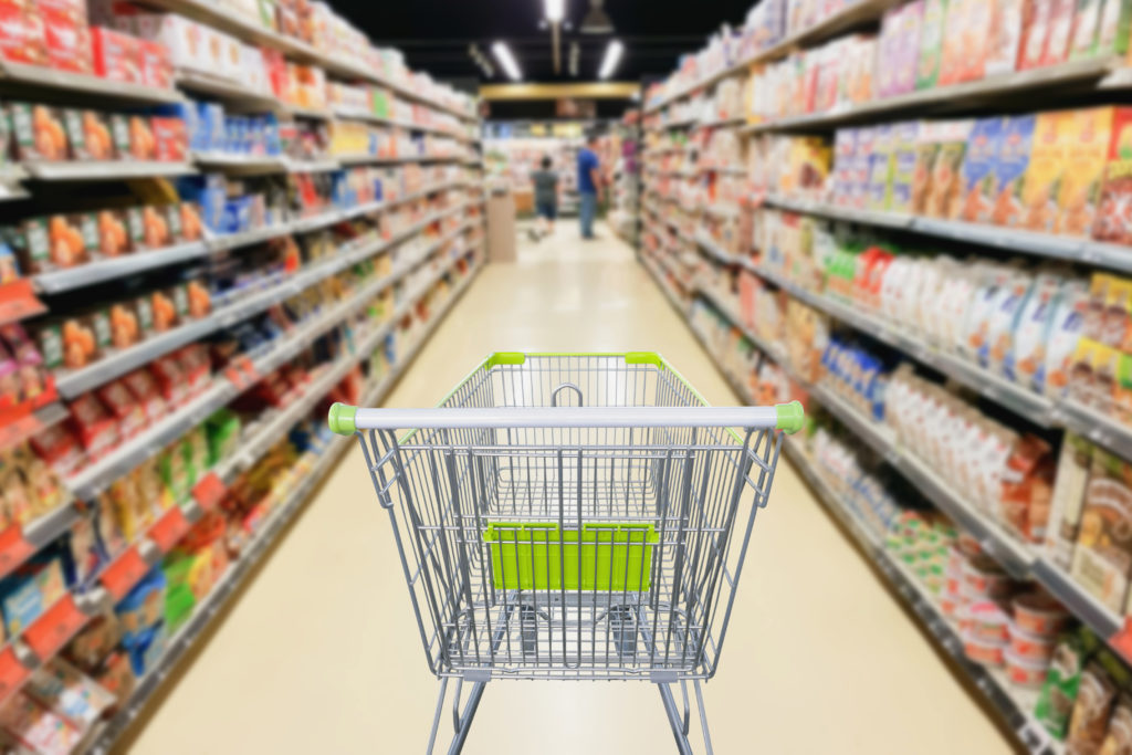 Empty shopping cart sitting in the middle of a grocery snack food aisle